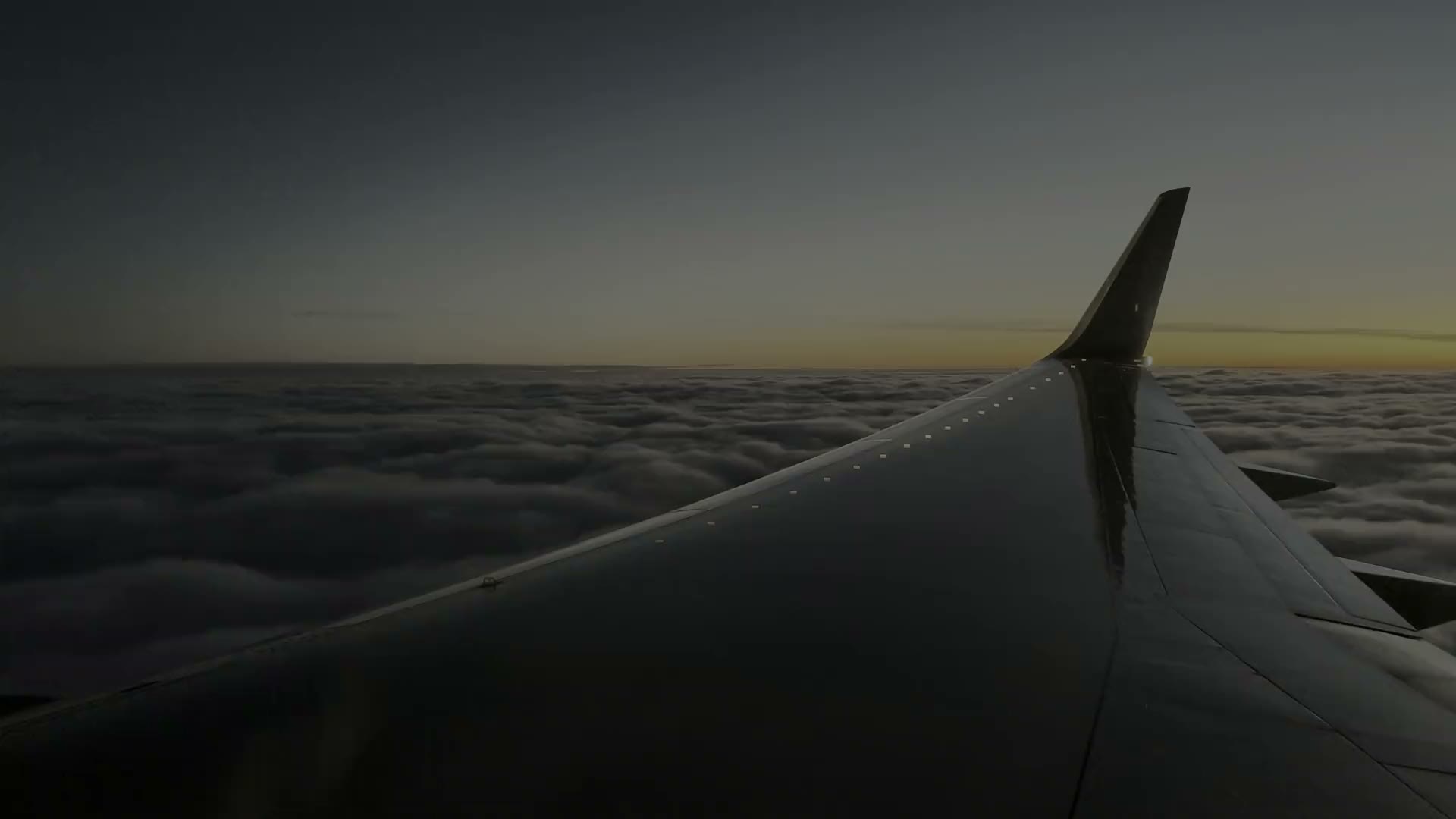 An aircraft wing above a sea of cloud at sunset